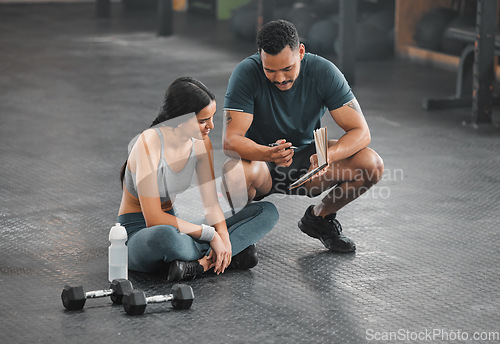 Image of Personal trainer, coach or fitness instructor helping an active and fit woman in the gym. Young female athlete sitting down and managing her workout routine or schedule with her exercising partner