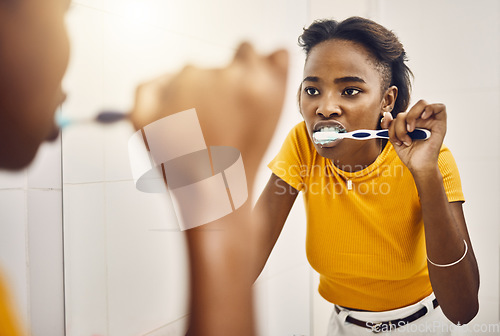 Image of Brushing teeth, dental hygiene and oral care with a young woman looking at her reflection in the bathroom mirror at home. Maintaining mouth, teeth and gum health with a daily toothcare routine