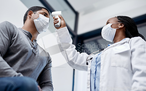 Image of Female doctor consulting a male covid patient, taking his temperature with infrared thermometer in hospital room or clinic. Man wearing mask and health care professional pointing medical equipment.