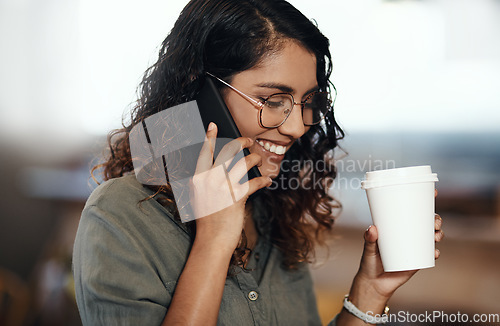 Image of Young woman talking on her phone, drinking coffee, and smiling in cafe shop. Lady wearing glasses, using technology to network and connect while enjoying a break from work.