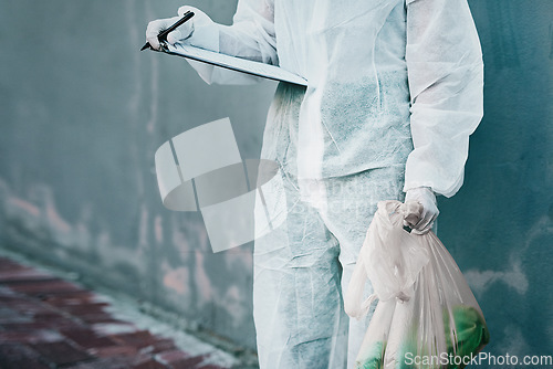Image of Forensic investigator collecting evidence on a murder scene on a street holding a plastic bag and wearing a hazmat suit. Crime researcher doing a scientific criminal investigation outdoors in a city