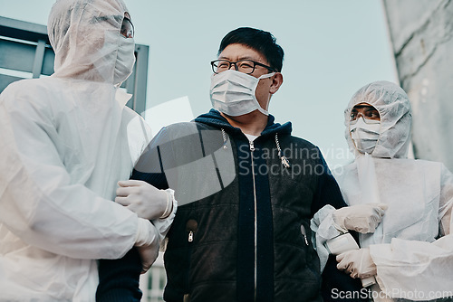 Image of Asian man breaking covid regulation getting taken away or arrested by healthcare workers wearing hazmat protective suits. Male removed for not following the rules or restrictions of the pandemic.