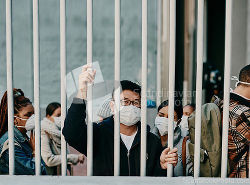 Image of Behind bars, lockdown and covid restrictions with a man wearing a mask during a pandemic and travel ban. Portrait of a male being locked out during the international or global corona virus outbreak