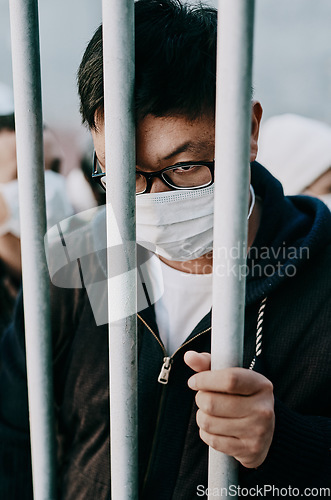 Image of Lockdown, isolation and covid travel ban with a man in a mask behind bars during an international pandemic. Corona virus restrictions, feeling like a prisoner or captive during a global shutdown