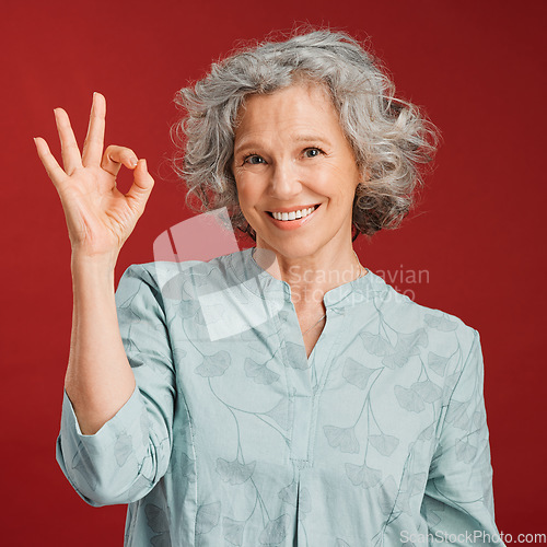 Image of Good, perfect and okay with a senior woman hand gesture or sign in support or positive backing in studio against a red background. Portrait of a mature female looking motivated, happy and smiling