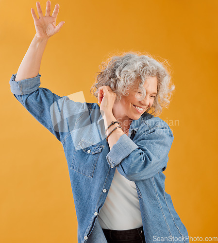 Image of Celebrating, partying and dancing mature woman, happy and cheerful senior making waving hand gesture and smiling. Elderly caucasian woman having fun while she dances against an orange background