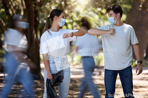 Image of Covid pandemic, social distancing and safety protocol or regulations outdoors in forest. Friends in motion greeting by bumping elbows, wearing mask for protection or prevention from corona virus.