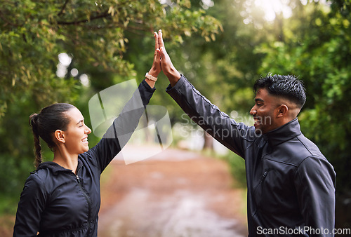 Image of Athletic couple high five while exercising in a park or forest, celebrating and winning before a run. Fit boyfriend and girlfriend bonding while keeping fit and healthy. Fun lovers being active