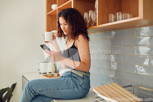Image of Woman texting, chatting on the phone while relaxed, carefree and sitting on kitchen counter. Young, relaxing and casual female student at home looking at social media, pictures or videos