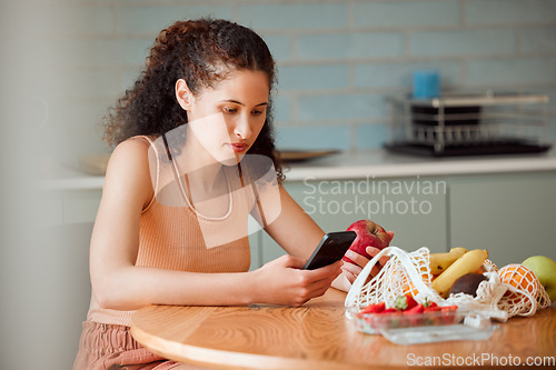 Image of Diet, healthy mindset and health food of a female doing apple research on a phone.Young woman nutritionist at home reading weight loss, cooking and nutrition holding online fruit in a kitchen