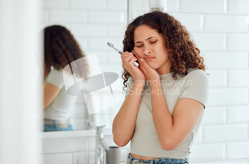 Image of Toothache, pain and sensitive teeth with a woman brushing her teeth in a bathroom at home. Young female with a cavity suffering from discomfort during dental hygiene routine. Lady with a sore mouth