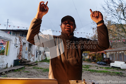 Image of A young man is entertaining a group of friends in the backyard of his house, becoming their DJ and playing music in a casual outdoor gathering