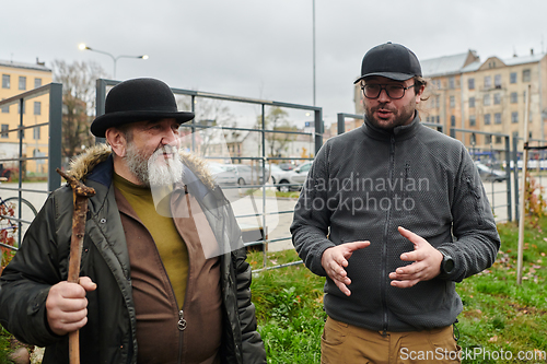 Image of In the picturesque garden of Riga, Latvia, a man engages in a heartfelt conversation with his older friend, enjoying the serene urban oasis amidst the bustling cityscape