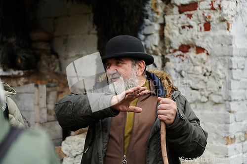 Image of An elderly man with a beard and a worn hat passionately imparts traditional values and cultural wisdom to others, embodying the essence of heritage preservation and storytelling.