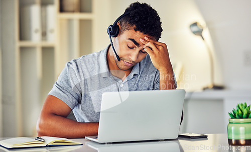 Image of Stressed, tired and frustrated call center agent feeling sick or ill in the office while working on his laptop. A worried and unhappy young telemarketing employee suffering from a headache and pain