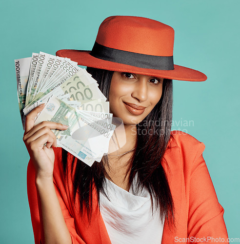 Image of Rich, successful and wealthy young woman holding cash money after winning competition, lottery or casino prize. Smiling, elegant and trendy female with pay reward against a blue studio background