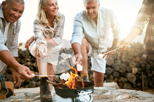 Image of Camping, hiking and adventure senior people melting marshmallows in a camp fire during a nature retreat or getaway outdoors. Happy retired or senior group of friends enjoying fun recreation activity