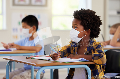 Image of Covid, education and learning with a student in class, writing and studying at a school while wearing a mask for safety. Young boy sitting in a classroom, listening to the lesson and taking notes