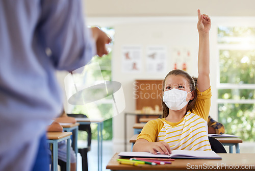 Image of Smart student with covid face mask asking teacher question about corona virus pandemic in a classroom or elementary school. Little girl child raising hand to answer healthcare related topic in class