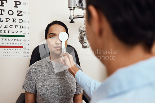 Image of Eye exam, vision testing at an optometrist with young woman and doctor. Opthamologist using an occluder to test eyesight before being fitted with glasses. Relaxed lady smiling, satisfied with service