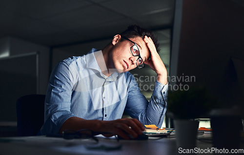 Image of Tired, stressed businessman suffering from headache, working late night in the office. Serious, frustrated and overworked corporate male with headache staring at his screen in the dark.