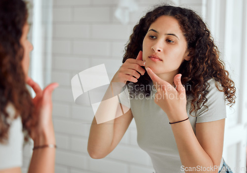 Image of Woman popping a zit during a skincare routine while in front of a mirror in the bathroom. Young Unhappy, upset or annoyed lady with a pimple targeting acne, dry skin or pimple on her face at home