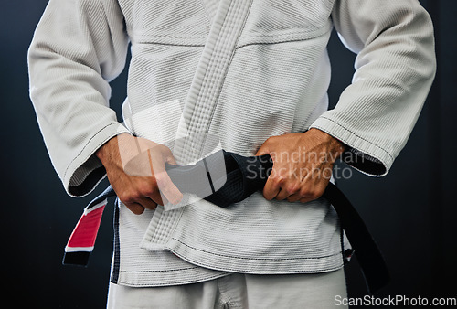 Image of . Professional karate master holding a black belt against a dark background in a dojo. Trainer, coach or leader prepared and motivated for training, fitness exercise and fight practice in a dojo.