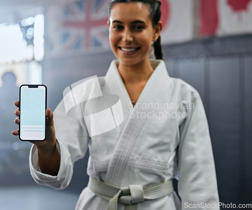 Image of Portrait of a female karate student holding tech with social media, looking active and fit at class. Blank screen on phone, showing a fitness app and training website while standing at a sports gym.