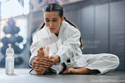 Image of . Female karate school student doing a warmup, stretch or exercise with serious, determine and focus before workout. Sports woman or coach leg stretching at a dojo studio, gym or martial arts club.