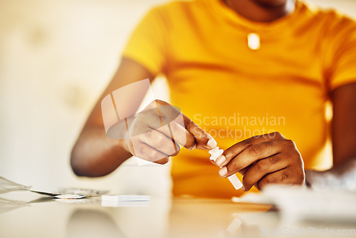 Image of Hands of African female with HIV and Aids at home blood self test kit sitting at a desk waiting to check for results. Closeup of young afro woman with medicine or pills for a medical condition.