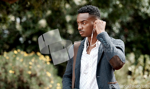 Image of A stylish, trendy and serious young man going to work while listening to music using earphones. A young African American male entrepreneur walking outdoors with nice style or fashion