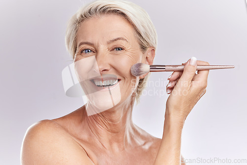 Image of Beauty, makeup and cosmetics of senior woman with a make up brush applying foundation, concealer or cosmetic product with a smile portrait. Happy blonde lady showing skincare for reducing wrinkles