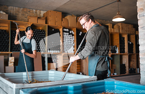 Image of Winemaker workers in the process of making wine with a wine press tool or equipment in a warehouse, winery or distillery. Woman, man or vintner people pressing juice of grapes for alcohol industry