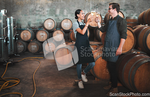 Image of Wine distillery owners cheers glasses in the cellar standing by the barrels. Happy and celebrating business owners or sommeliers enjoying chardonnay or sauvignon blanc inside a winery