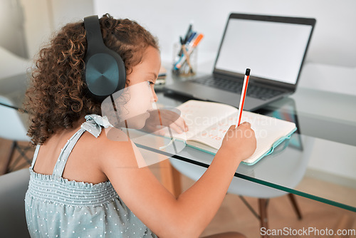 Image of Homeschooling by a smart and clever little girl attending online or virtual class using a laptop and headphones. A young child writing and working or doing homework at home listening to music