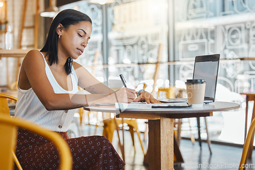 Image of Student writing, taking notes or doing a project assignment in cafe or restaurant using laptop and notebook. Young woman taking an online education class or doing study work, learning in coffee shop.