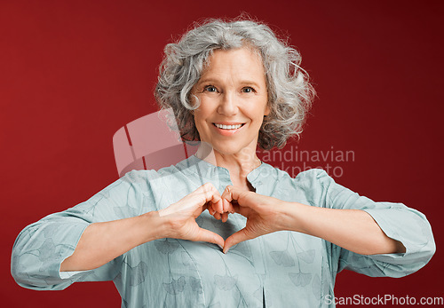 Image of Love, heart and health retired woman with loving emoji sign, icon or symbol showing care or affection on red valentines day studio background. Grey, senior or pensioner with a trendy emoticon pose