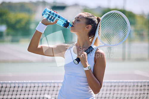 Image of Fit and active tennis player drinking water from a bottle after practicing, training and playing on a sports court or club. Thirsty professional sportswoman hydrating while holding a racket outside