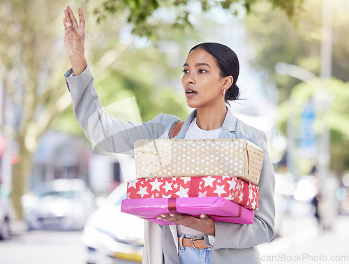 Image of Woman holding gift and calling for a taxi in the street for travel to a birthday, anniversary or congratulation party. City girl standing in the road after shopping for a present for friend or family