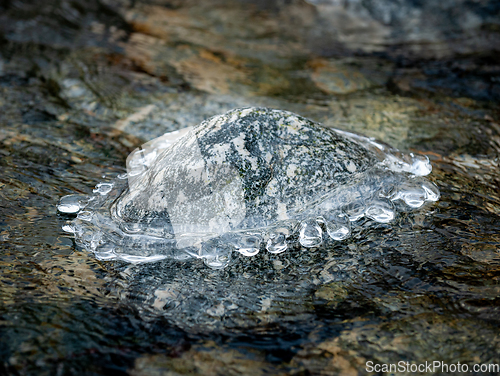 Image of Frozen Rock Encased in Ice Amidst a Partially Thawed Stream in W