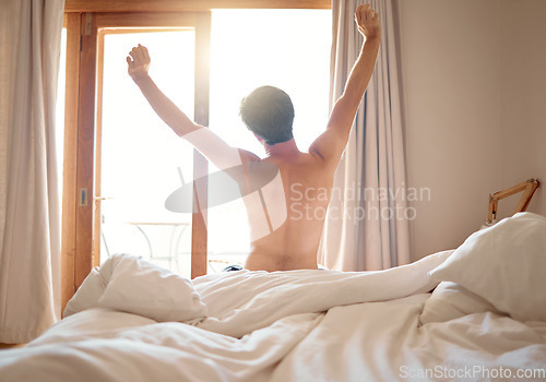 Image of Man in nude stretching after night sleep in bed, waking up to morning sunrise in bedroom and feeling excited for day at home. Back of naked male person relaxing after nap or rest in apartment house