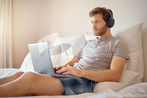 Image of Man working or typing on laptop and listening to music with headphone in bed at home. Remote worker streaming podcast online while reading and send work email on wireless tach in the bedroom alone