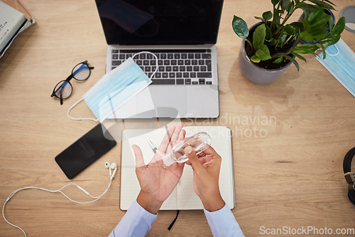 Image of Covid, sanitizer and personal safety with a business person or employee sanitizing hands and working at a desk in an office. Healthcare, hygiene and cleaning at work during the corona virus pandemic