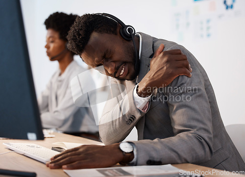 Image of Pain, injury and hurt call center agent holding his shoulder in agony while working in the office. Young African American male customer service consultant suffering from a painful arm