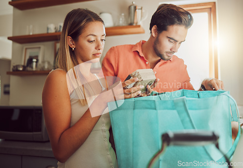 Image of Groceries, plastic free and healthy couple unpacking after returning home from a shopping trip. Serious man and woman with reusable bag with food and ingredients while reading nutritional labels