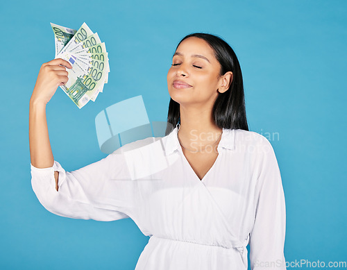 Image of .Money, wealth and rich woman holding fan of cash and cooling herself, ready to blow or spend it all. Female lottery winner embracing luck, success and win in the studio on a blue background.