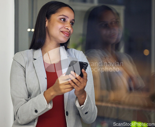 Image of Thinking, phone and smiling woman texting, browsing the internet or using a mobile app with good network while working late at night. Hardworking entrepreneur checking investment growth online