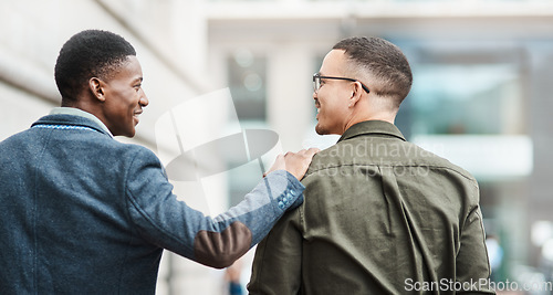 Image of Two young businessmen smiling, talking and walking through the city together, excited for their new project. Happy multiracial coworkers strolling with his hand on his friends shoulder while laughing