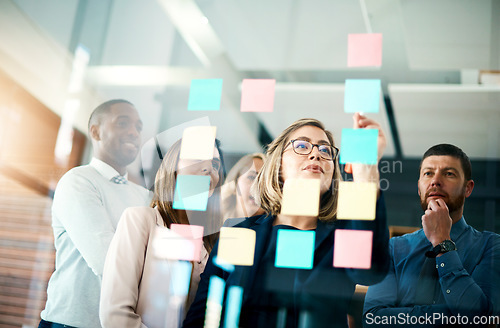 Image of Group of business people talking about the notes on the glass wall in the office. Corporate meeting and discussion with the team about new ideas. Brainstorming logistics and strategy together.