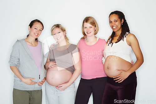 Image of Pregnant, mother and friends with women in studio against a white background feeling happy with a smile. Pregnancy, health and wellness with positive female parents holding their abdomen together